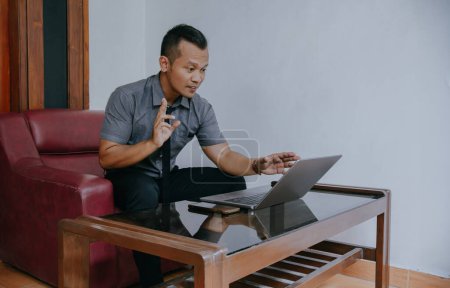 Joven hombre de negocios centrado en el trabajo en el ordenador portátil, utilizando videollamada con el cliente en el ordenador portátil. Joven hombre indonesio concentrándose en dar clases de educación en línea conferencias, consultoría con los clientes.