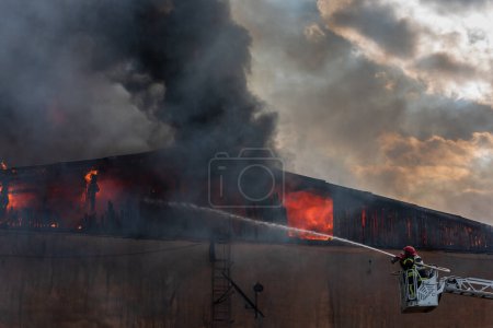 Photo for Severe fire in a storage factory. There was a fire in a warehouse. The flames engulfed the roof of the building. Burning produces heavy smoke. - Royalty Free Image