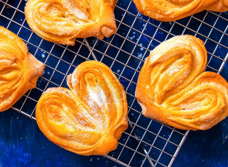 Photo for Homemade sugar buns on a cooling rack with sugar for sprinkling. Palmiers, elephant ear, puff pastry cookie. - Royalty Free Image