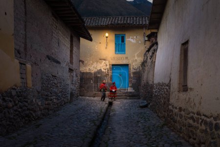 Foto de Una pintoresca calle empedrada en el crepúsculo con el canal de riego distintivo, Ollantaytambo, Cusco, Perú. Ejemplo de supervivencia de callejuelas incas originales. - Imagen libre de derechos
