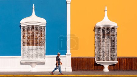 Foto de Hombre local que pasa frente a la arquitectura colonial tradicional con grandes barandillas pintadas de blanco y paredes de colores pastel, Trujillo, Perú - Imagen libre de derechos