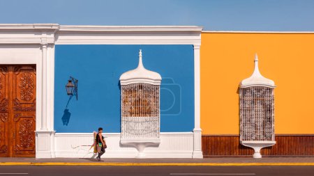 Foto de Cometa vendedor pasando por delante de un edificio de color con blanco pintado, delicadas barandillas de ventana y puertas de madera con incrustaciones, Trujillo, Perú. - Imagen libre de derechos
