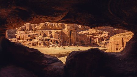 Téléchargez les photos : Vue de la rue des façades à travers une fenêtre de grotte avec des dizaines de tombes plus petites et une caravane de chameaux, Petra, Jordanie - en image libre de droit