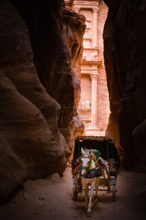 Foto de El templo de Tresaury (Al Khazneh) enmarcado por la pared del Siq con un carro de caballos locales utilizado para el transporte de turistas, Petra, Jordania - Imagen libre de derechos