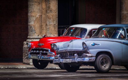 Photo for Old 1950s cars stopped at a city crossroads in Havana in front of a crumbling colonial building - Royalty Free Image