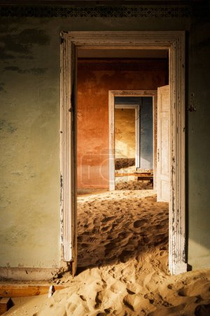 Interior de un edificio abandonado en Kolmanskop, Namibia, envuelto en arena e iluminado por la cálida luz del desierto de Namib. Fundada en 1908 para la exploración de diamantes, la ciudad fue abandonada en 1956.