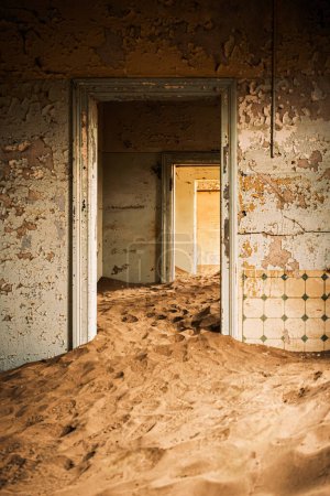 Foto de Interior de un edificio abandonado en Kolmanskop, Namibia, envuelto en arena e iluminado por la cálida luz del desierto de Namib. Fundada en 1908 para la exploración de diamantes, la ciudad fue abandonada en 1956. - Imagen libre de derechos