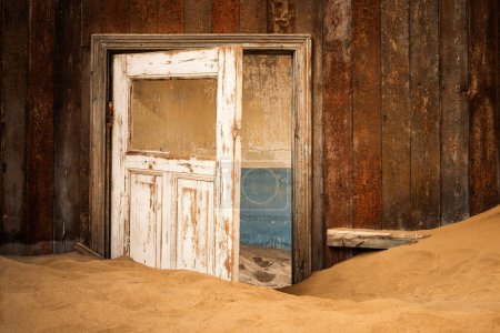 Foto de Interior de un edificio abandonado en Kolmanskop, Namibia, envuelto en arena e iluminado por la cálida luz del desierto de Namib. Fundada en 1908 para la exploración de diamantes, la ciudad fue abandonada en 1956. - Imagen libre de derechos