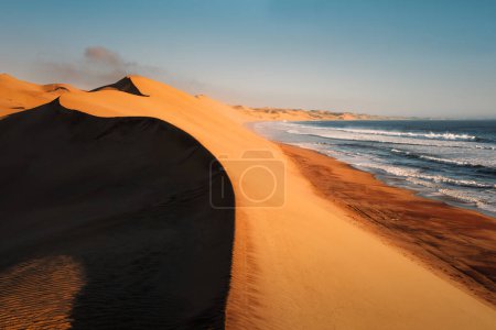 Die geschwungenen Dünen der Namib-Wüste fallen am Sandwich Harbor südlich von Walvisbucht im Namib-Naukluft-Nationalpark in Namibia in den kalten Atlantik..