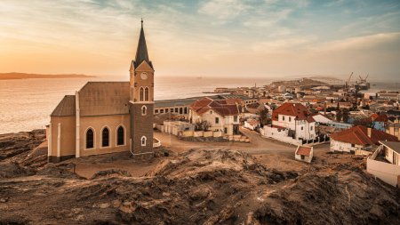 Panoramic view of Luderitz, Namibia, showcasing the Felsenkirche, the historic city Lutheran Church, and the German-style houses and buildings extending towards the port and the Atlantic Ocean.