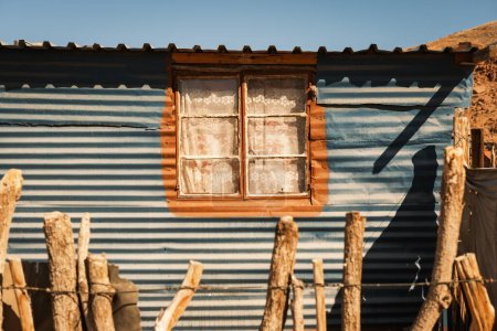 Hausfenster im Stammesdorf Damara in der Nähe von Twyfelfontein, Kunene, Namibia. Trotz der Verwendung schlechter Materialien ist das Fenster mit Vorhängen und einem bemalten Rahmen dekoriert.