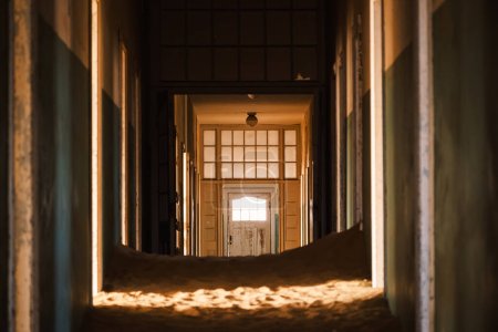 Interior of the abandoned hospital in Kolmanskop, Namibia, engulfed by sand and lit up by the warm light of the Namib Desert. Founded in 1908 for diamond exploration, the town was abandoned in 1956.