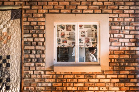 Foto de Mujer local detrás de la ventana ocupada preparando el desayuno para los clientes del albergue, cerca de Kamanjab, Región Kunene, Namibia - Imagen libre de derechos