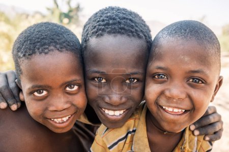 Foto de Foto de la cabeza de los niños del árbol Himba sonriendo cerca del río Kunene en las cataratas Epupa, Namibia. Los Himba son una tribu africana semi-nómada que ha confiado en el río durante siglos.. - Imagen libre de derechos