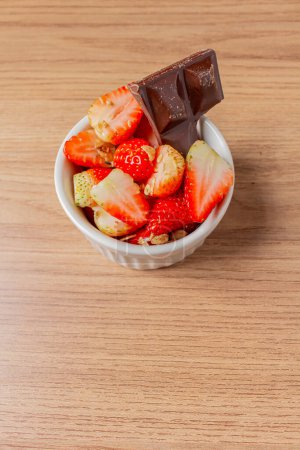 Photo for Strawberries in bowl and a piece of chocolate on a wooden background. - Royalty Free Image