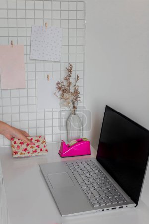 Foto de Mano femenina poniendo cuaderno floral cerca del ordenador portátil y artículos de papelería en el escritorio blanco. Concepto empresarial - Imagen libre de derechos