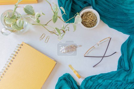 Foto de Espacio de trabajo plano con planificador de mostaza, clips de papel de oro, cinta washi, pasador de pelo, bufanda verde y gafas - Imagen libre de derechos