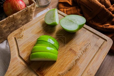 Foto de Composición otoñal con manzanas verdes en rodajas sobre tabla de madera, cesta de paja con manzanas rojas y suéter marrón - Imagen libre de derechos