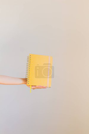 Téléchargez les photos : Main de femme tenant un cahier de moutarde. Concept minimaliste - en image libre de droit