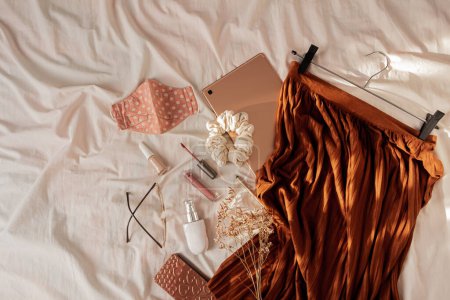 Foto de Composición femenina de moda con hermosa falda elegante, mascarilla, tableta de oro rosa, gafas y cosméticos. sobre manta de lino blanco. - Imagen libre de derechos
