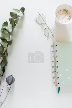 Foto de Planificador, taza de café y leche, hojas de eucalipto, vasos, colador de té sobre fondo blanco. Plano, vista superior, espacio para copiar. - Imagen libre de derechos