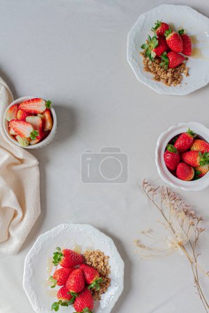 Foto de Las fresas en los platos con la granola y la miel, también las fresas en la escudilla y el azucarero sobre el fondo blanco. - Imagen libre de derechos
