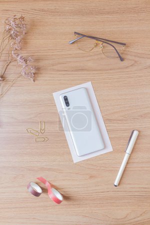 Photo for Workspace with smartphone, glasses, wildflower, pen, washi tapes and paper clips on wooden background. Flat lay, top view - Royalty Free Image