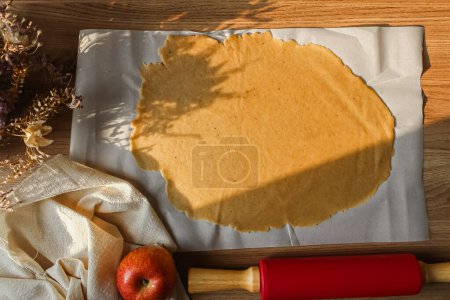 Foto de Vista superior de la masa laminada sobre papel de hornear con rodillo y manzana roja - Imagen libre de derechos