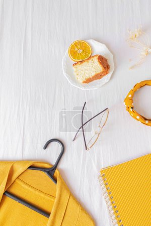 Photo for Top view of home office desk frame with laptop, orange piece of cake, cardigan, glasses and planner on white background. - Royalty Free Image