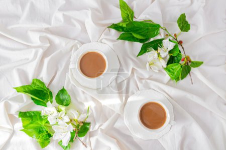 Téléchargez les photos : Tasse à lait et café avec fleurs blanches et feuilles de mûrier sur fond de lit salissant. - en image libre de droit