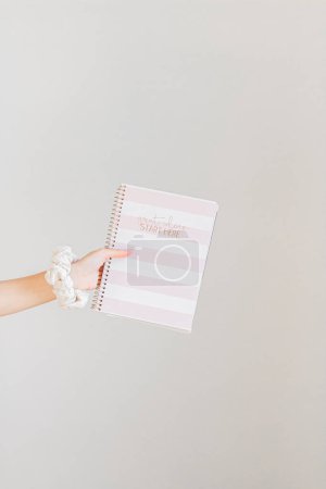 Photo for Female hand holding pink planner with a scrunchie on the wrist - Royalty Free Image
