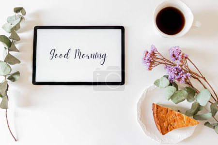 Foto de Frase "buenos días" en una tableta, marco floral y composición del desayuno sobre fondo blanco. Concepto de mañana lenta. - Imagen libre de derechos