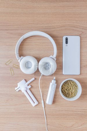 Photo for Workspace with headphone, paper cutter, eletric eraser, paper clips and smartphone on wooden background. - Royalty Free Image