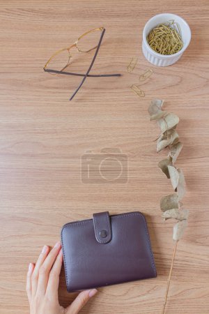 Foto de Área de trabajo minimalista de escritorio de oficina con gafas, billetera, rama de eucalipto seco, clips de papel dorados sobre un fondo de madera. Asiento plano, vista superior. Concepto de finanzas. - Imagen libre de derechos