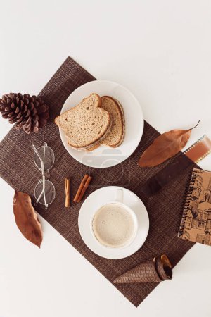 Photo for Top view of cup of coffee with homemade sliced bread, cinnamon sticks and dried leaves around. - Royalty Free Image