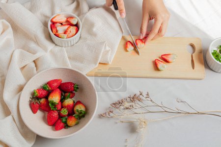 Foto de Joven hembra manos cortando algunas fresas en la tabla de cortar sobre fondo estilizado. - Imagen libre de derechos