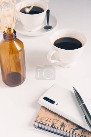 Téléchargez les photos : Deux tasses de table blanche café avec smartphone et bloc-notes - en image libre de droit