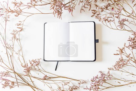 Téléchargez les photos : Cadre rond en fleurs lilas sur fond blanc avec bloc-notes en papier blanc ouvert. Couché plat, vue du dessus. - en image libre de droit
