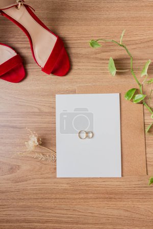 Photo for Elements of wedding decor. Wedding rings, wedding green plants, red high heels, and invitation. Indoors, close-up. Wedding preparation concept. - Royalty Free Image