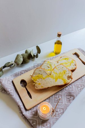 Photo for White bread slices with olive oil on the top on wooden board with candle and an eucalyptus dried leaves, - Royalty Free Image