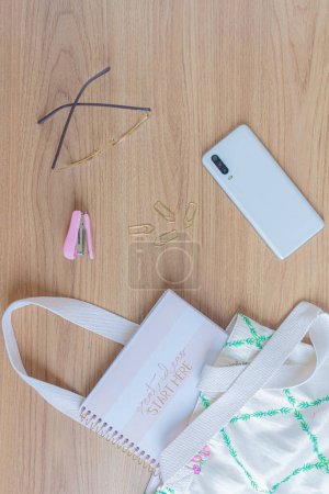 Photo for Neutral fashion composition with female accessories and stationary supplies on wooden table. Cotton bag, notebook, glasses and smartphone . Minimal lifestyle concept. - Royalty Free Image