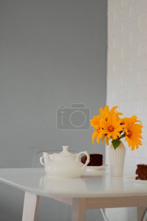 Foto de Ramillete de girasoles amarillos en jarrón sobre la mesa con trozos de pastel y tetera - Imagen libre de derechos