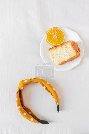 Foto de Composición del desayuno con pastel en plato blanco y diadema sobre fondo textil blanco. Piso tendido, vista superior - Imagen libre de derechos