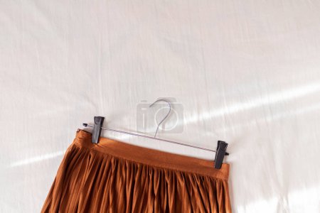 Téléchargez les photos : Composition des femmes de mode avec belle jupe plissée marron élégant sur couverture en lin blanc. Couché à plat, vue de dessus. Concept de mode. - en image libre de droit