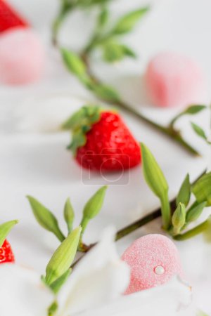 Téléchargez les photos : Composition alimentaire printanière avec branche de fleurs, fraises et bonbons sur fond blanc - en image libre de droit