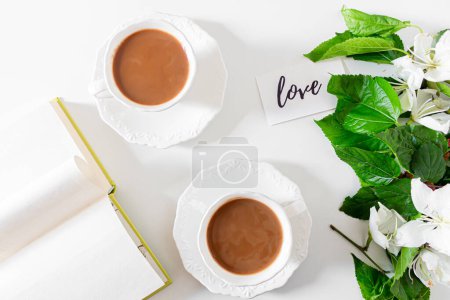 Téléchargez les photos : Tasse de café et de lait, carte avec le message : "amour", fleurs blanches et feuilles de mûrier sur fond blanc. Concept de printemps. - en image libre de droit