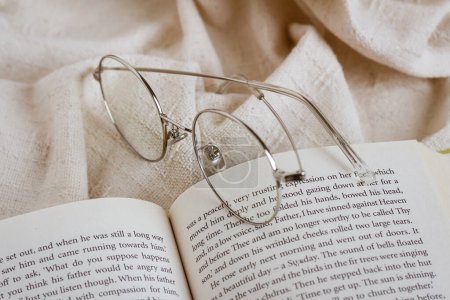 Téléchargez les photos : Livre ouvert avec des lunettes sur drap de lit - en image libre de droit
