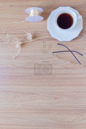 Photo for Cup of coffee, pen, paper clips, glasses, string and dried flowers and leaves on a wooden background. Flat lay, top view. - Royalty Free Image