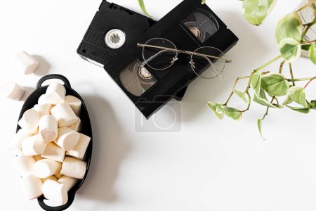 Photo for Video cassette, plant branches and marshmallows on white background. Flat lay, overhead view, top view. Old-fashioned date concept. - Royalty Free Image