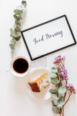 Photo for Phrase"good morning" on a tablet, floral frame and breakfast composition on white background. Slow morning concept. - Royalty Free Image